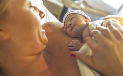 Frau lächelt frisch geborenes Baby an, das sie im Arm hält