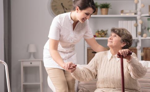 Pflegekraft hilft alter Dame beim Aufstehen
